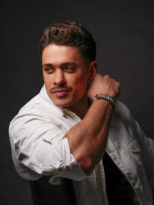 Männliches Model posiert im Studio, dunkler Hintergrund, seitlich sitzend, Lächeln, Fotograf Aachen