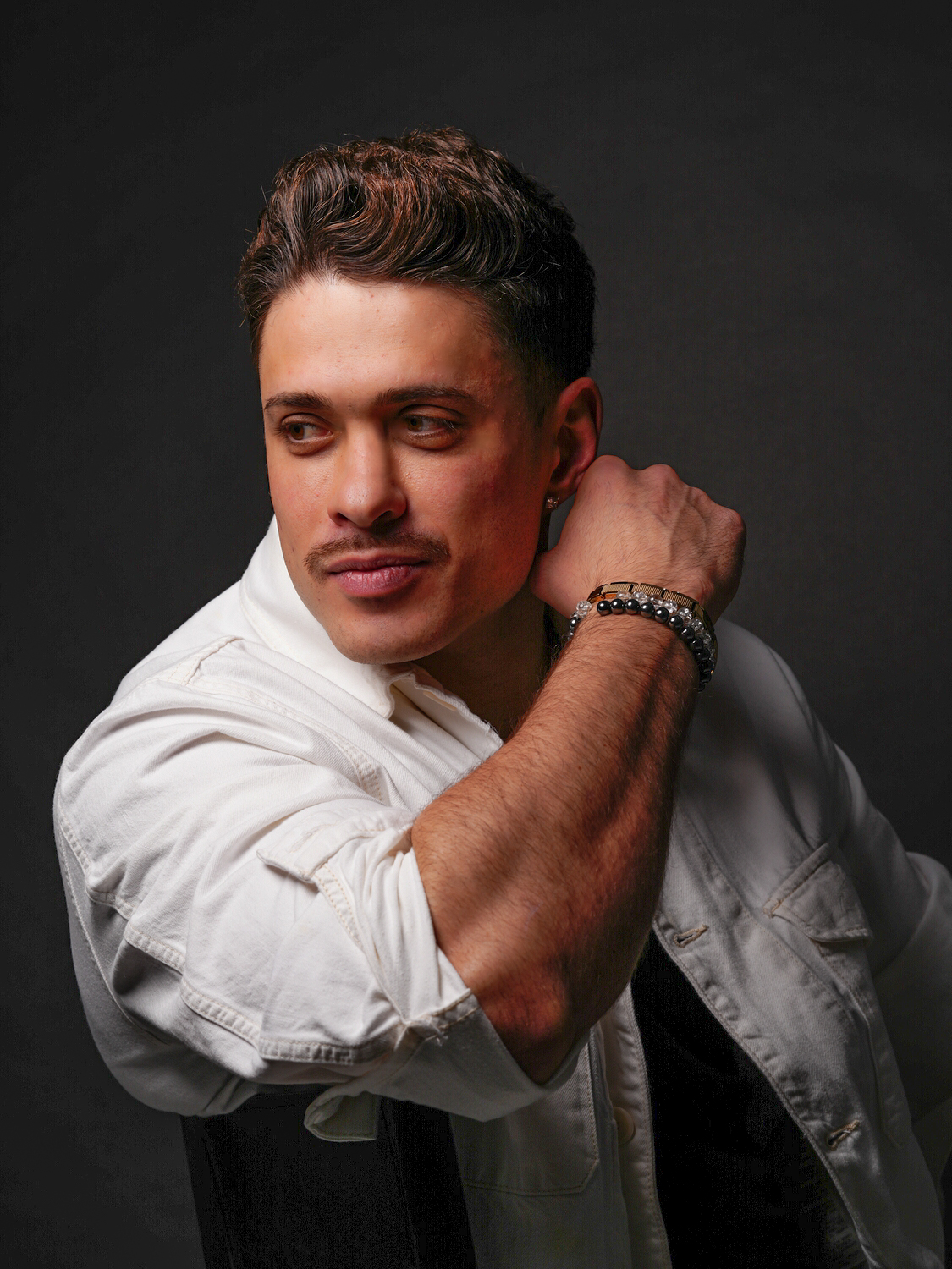 Männliches Model posiert im Studio, dunkler Hintergrund, seitlich sitzend, Lächeln, Fotograf Aachen